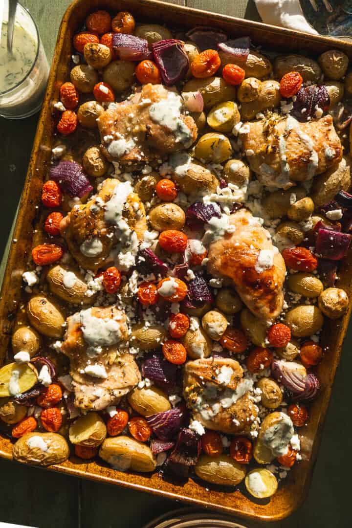 Greek chicken sheet pan dinner with yogurt sauce and feta on top.