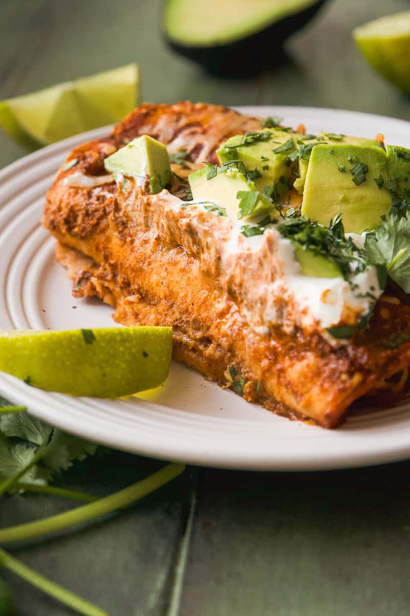 Creamy chicken enchiladas on a plate with avocado and greek yogurt on top.