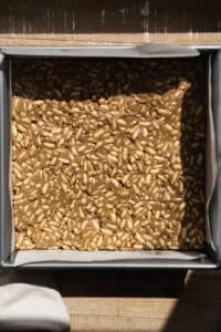 Sunflower butter crunch bars pressed into a square dish with parchment paper.