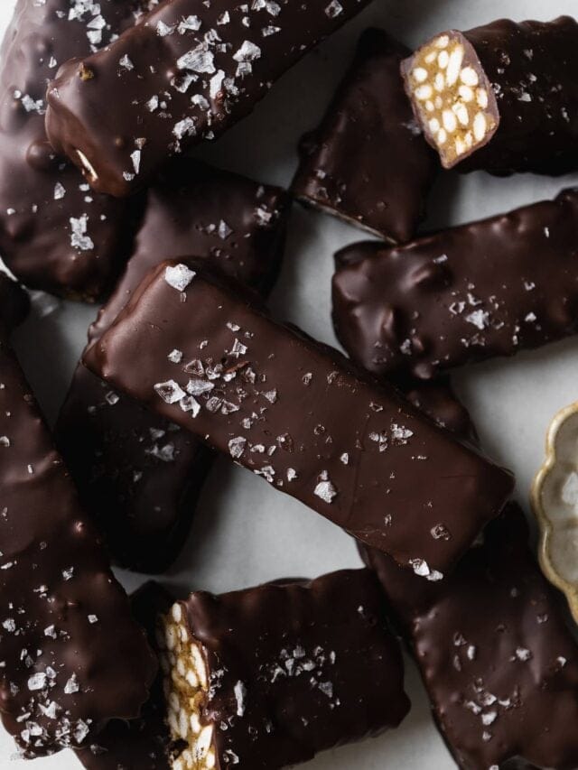 Chocolate coated crunch bars with sea salt on top scattered on parchment paper.