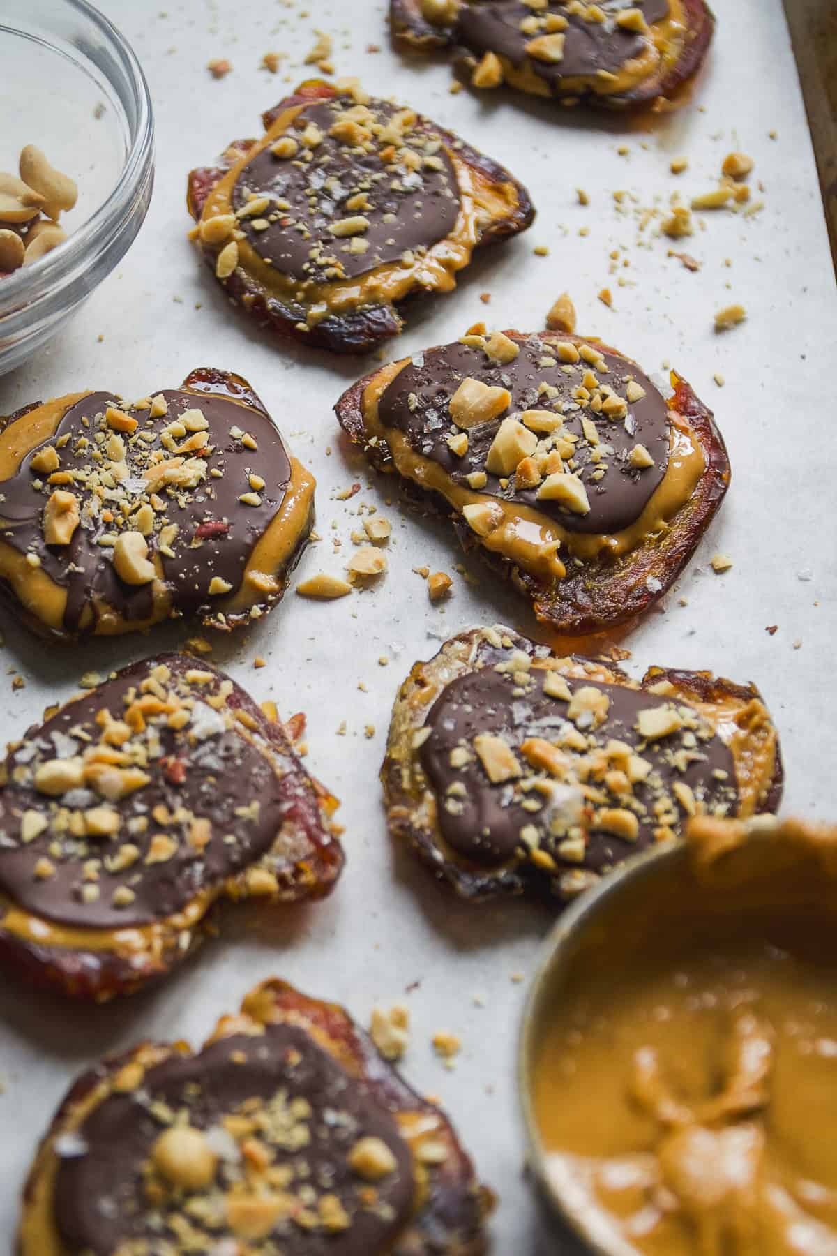 Smashed dates with peanut butter and chocolate on parchment paper.