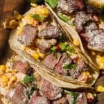 Steak tacos with corn salad on a wooden cutting board.