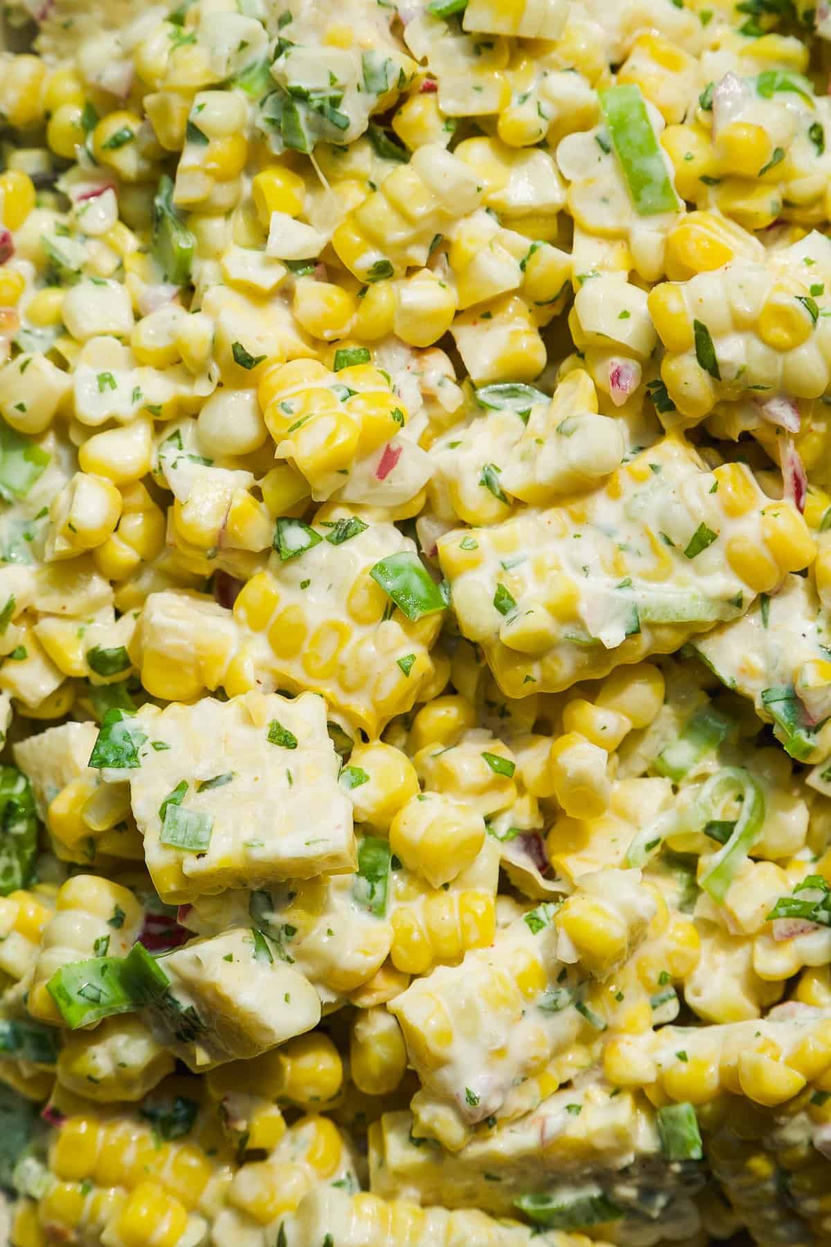 Close-up of creamy corn salad with chopped green onions, cilantro, and red onion mixed in a mayonnaise-based dressing.