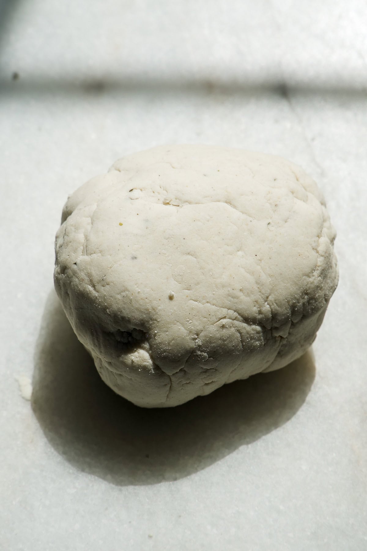 A close-up of a ball of dough resting on a white marble surface in natural light.