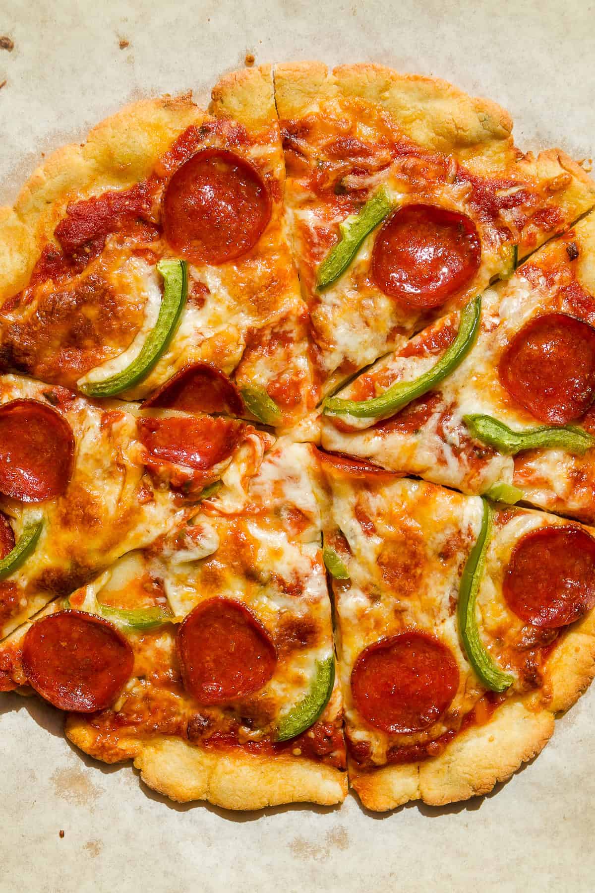 A baked pizza with eight slices, topped with melted cheese, pepperoni, and green bell pepper strips, on a parchment paper background.
