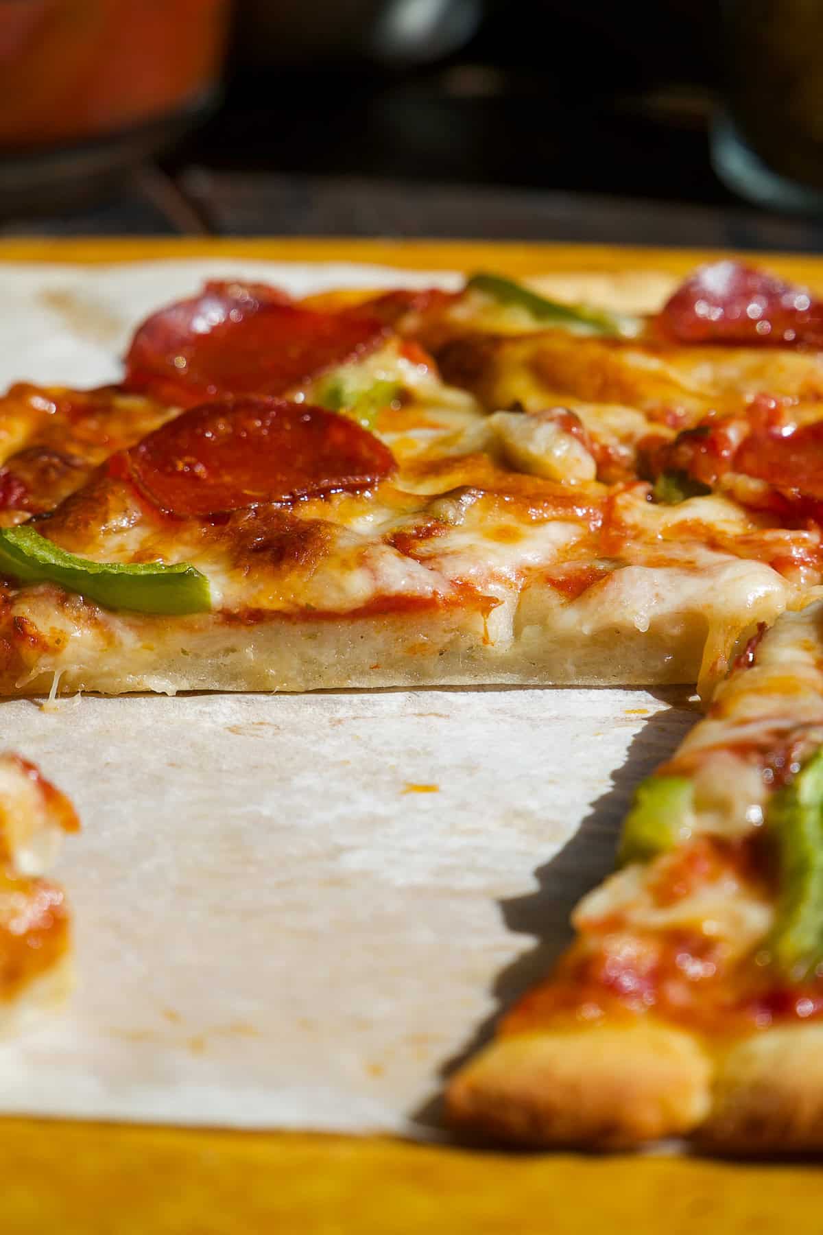 Close-up of a freshly baked pizza with melted cheese, pepperoni slices, and green bell peppers on a golden crust, with one slice partially removed from the main pizza.
