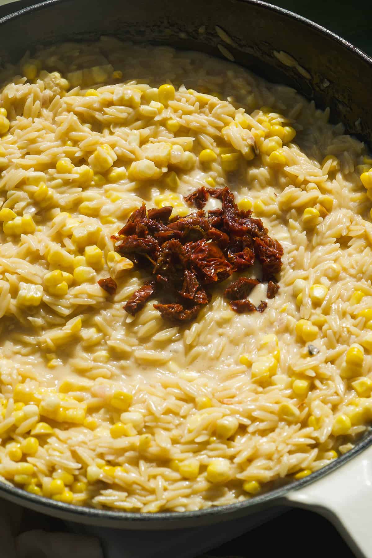 Creamy corn orzo pasta mixed with sweet kernels, topped with a small pile of chopped sun-dried tomatoes, served in a large pan.