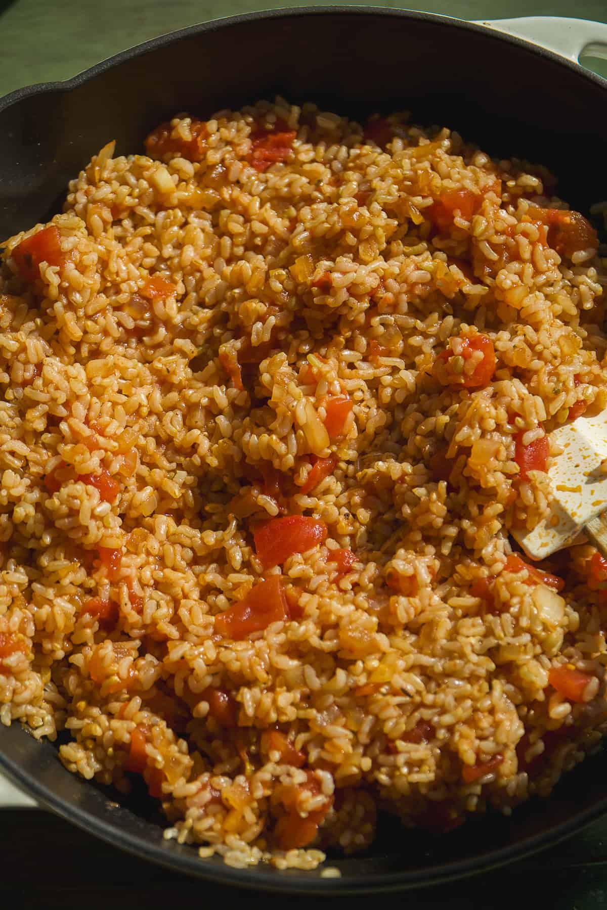 A close-up of a skillet filled with cooked rice mixed with diced tomatoes and seasonings, stirred with a white spatula—the perfect base for flavorful Mexican rice bowls.