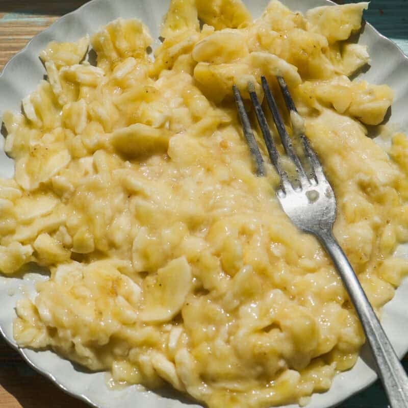 A white plate with mashed bananas and a silver fork rests on a rustic wooden surface, ready for your next batch of banana bread baked oats.