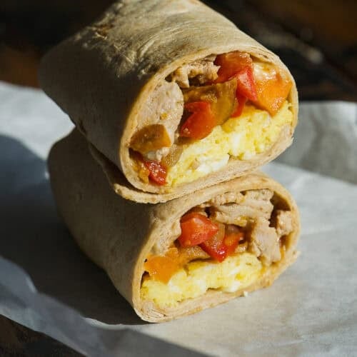 A breakfast burrito cut in half, stacked with visible layers of eggs, peppers, and meat inside a tortilla, placed on parchment paper—perfect for making ahead as freezer breakfast burritos.
