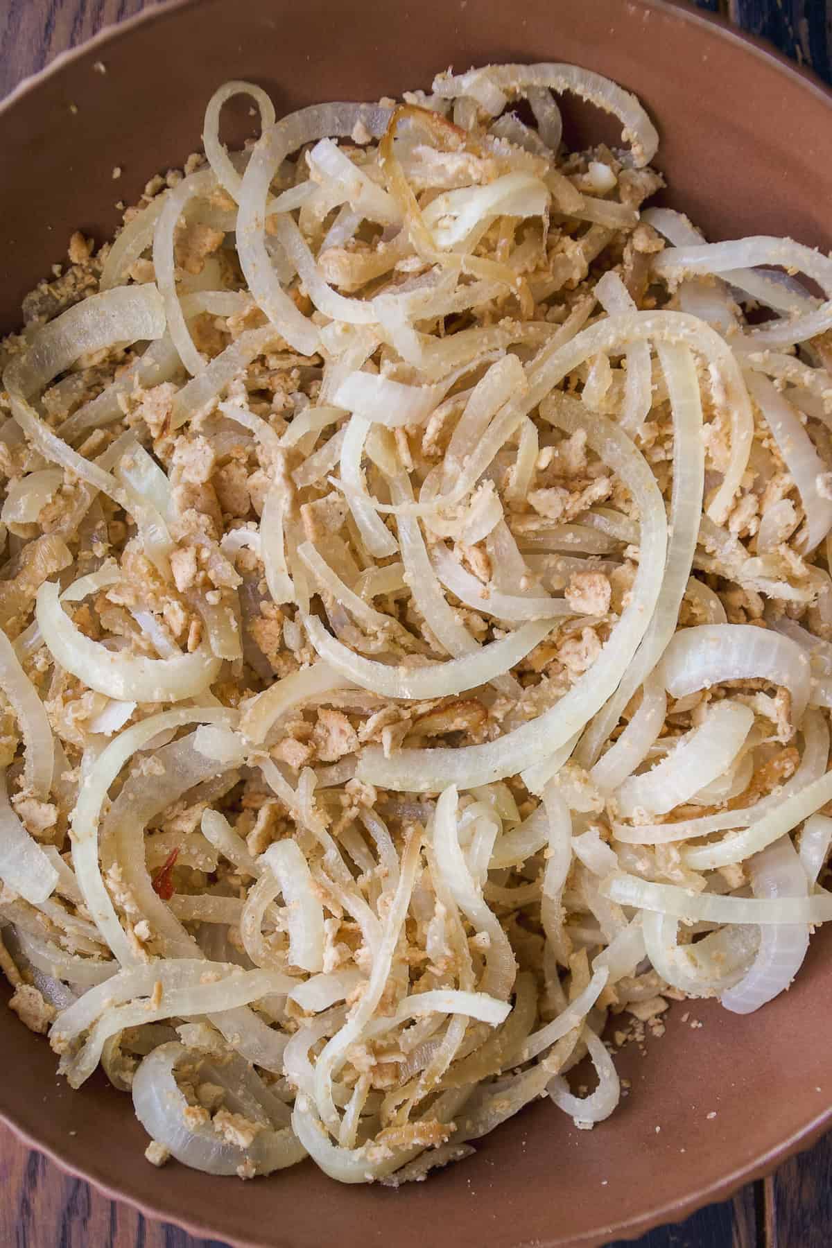 Thinly sliced onions mixed with crushed peanuts are served in a brown bowl, creating a rustic and simple dish. The mixture appears lightly seasoned and has a slightly translucent, golden appearance.