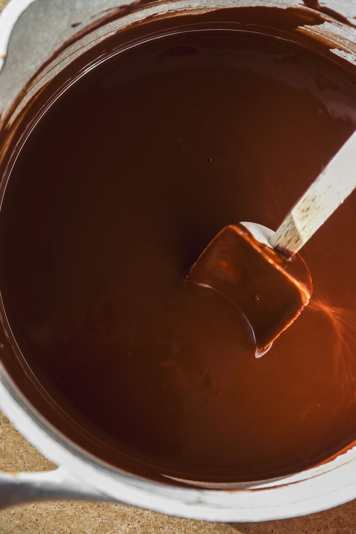 A spatula stirring smooth, melted chocolate in a metal bowl.