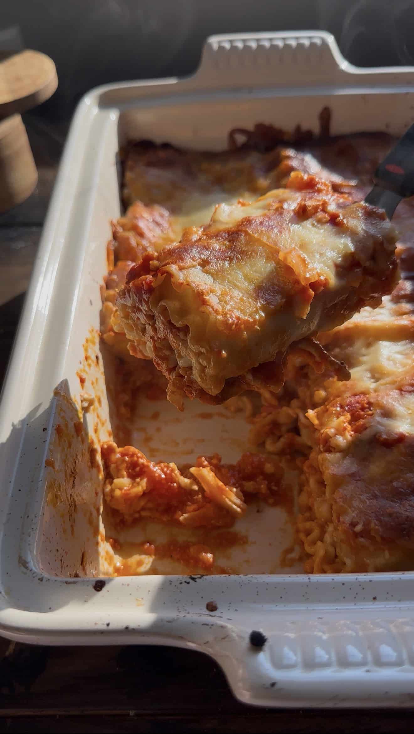 A close-up of cheesy, saucy lasagna roll ups being lifted from a white baking dish, with golden melted cheese and visible layers of pasta and red sauce.