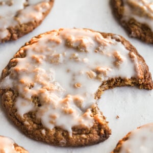 A close-up of frosted cookies on a white surface, with one cookie in the foreground showing a large bite taken out of it.
