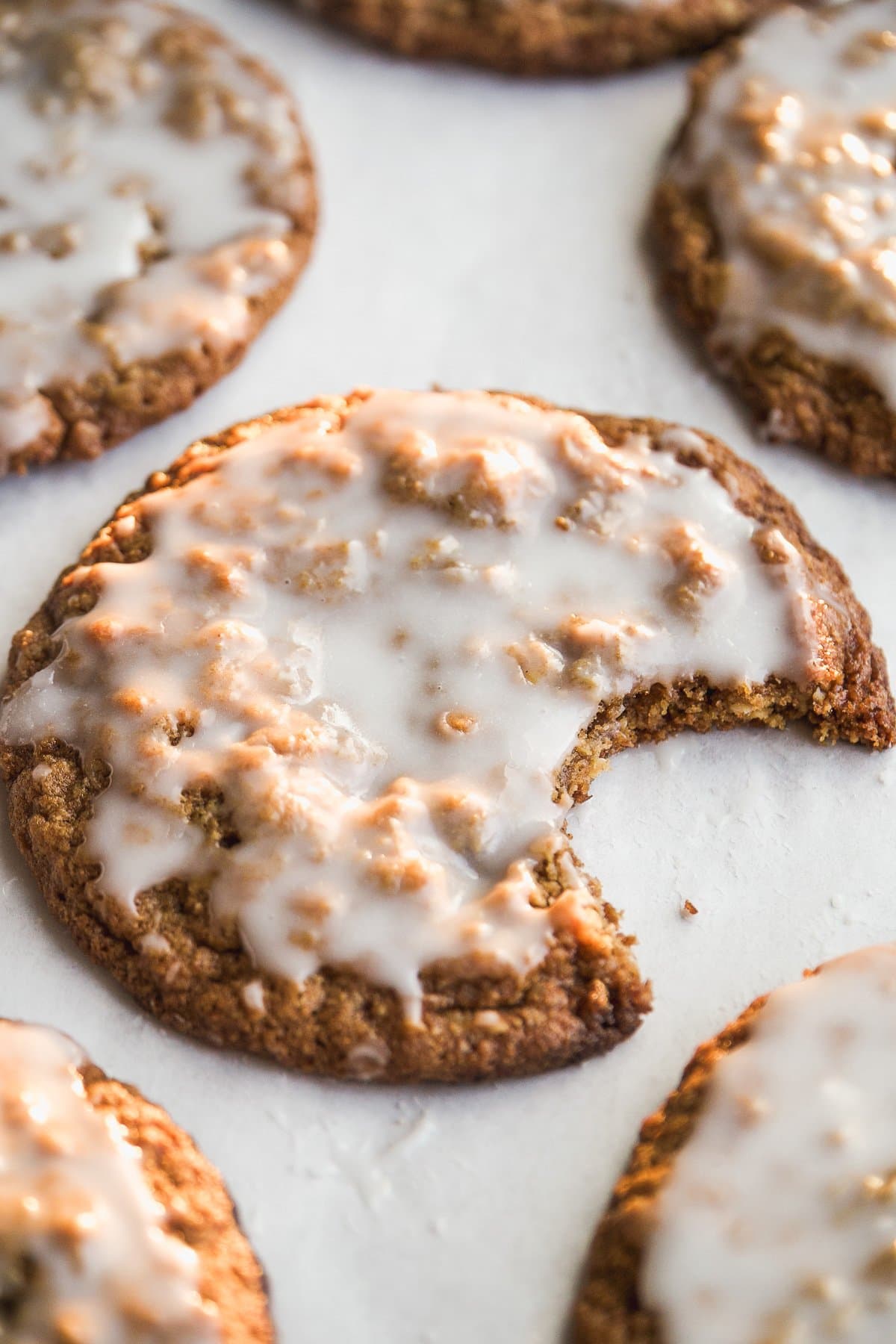 A close-up of frosted cookies on a white surface, with one cookie in the foreground showing a large bite taken out of it.