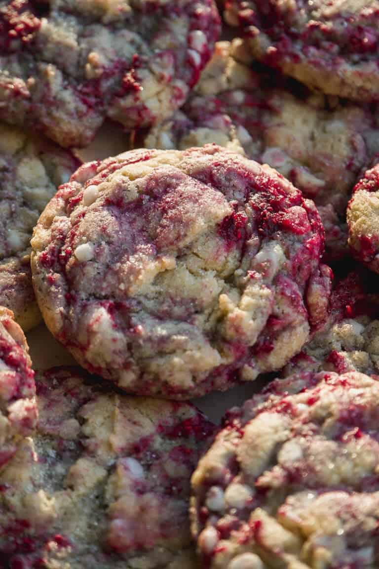 Close-up of several cookies with a marbled appearance, featuring swirls of red berry filling and white chocolate chips, giving a rustic and textured look.