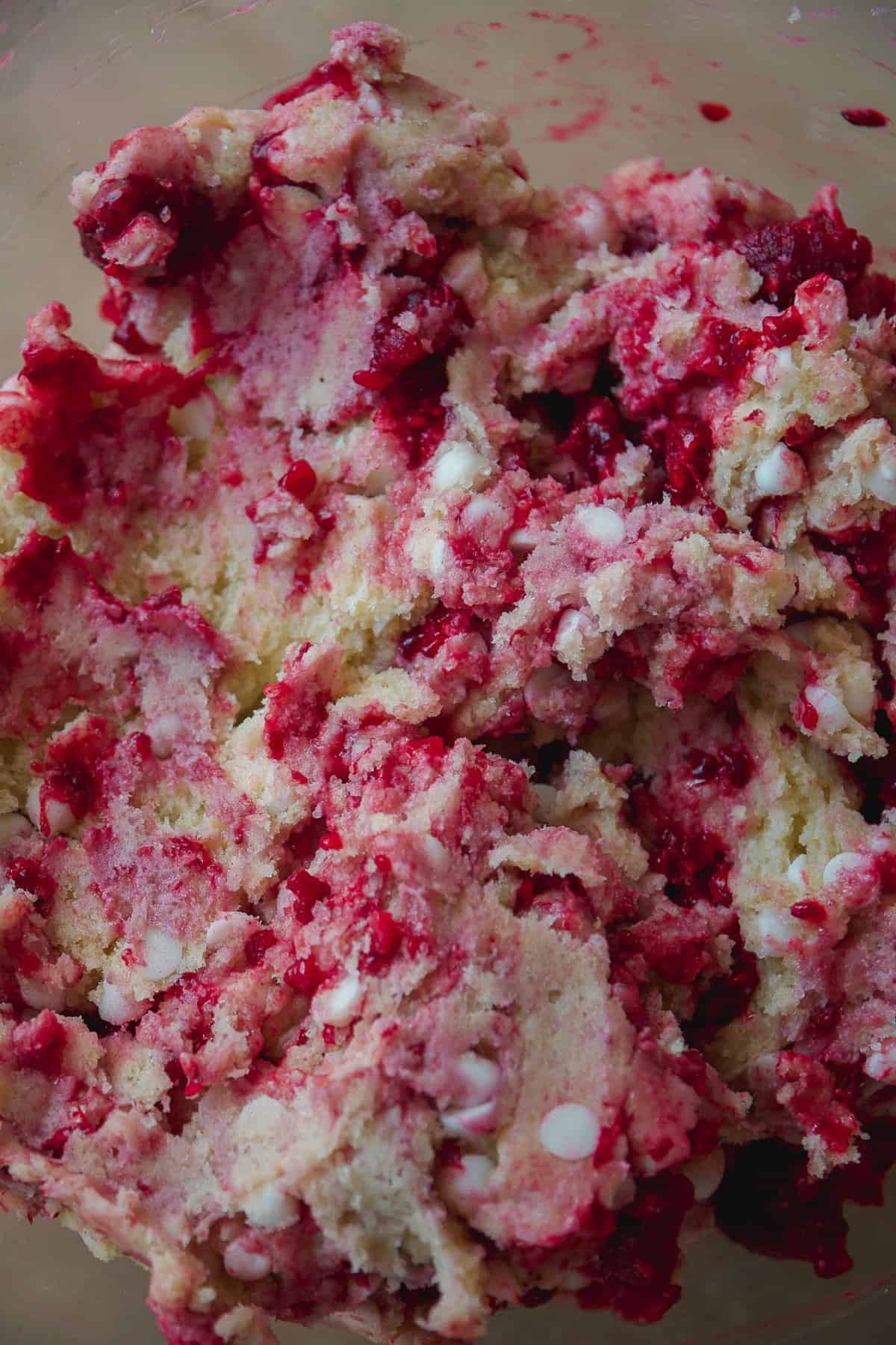 Close-up of cookie dough mixed with bright red raspberries and white chocolate chips, showing a chunky and colorful texture.
