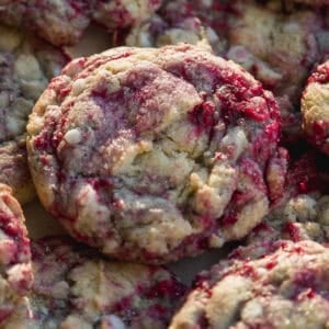 A close-up of several raspberry cookies with white chocolate chips, showing a marbled pattern of red raspberry and golden cookie dough.
