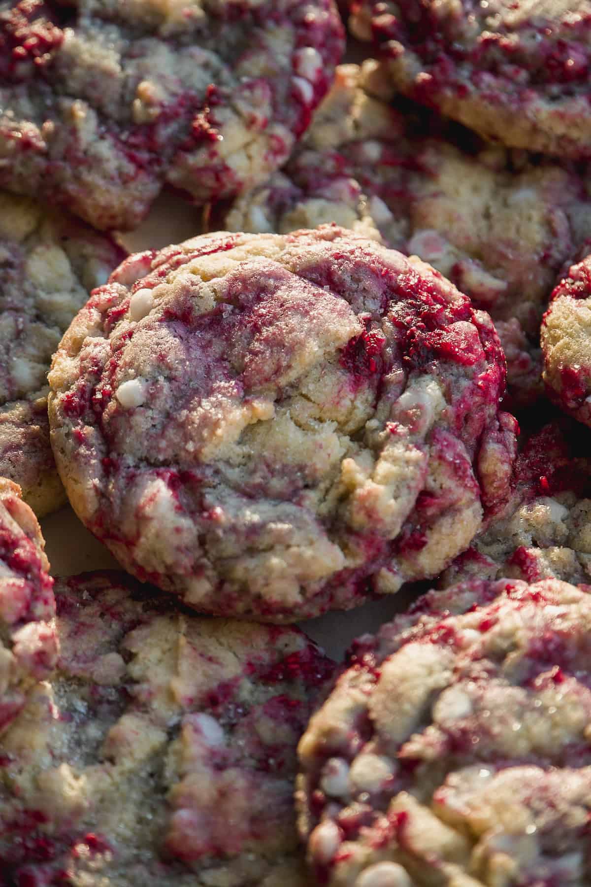A close-up of several raspberry cookies with white chocolate chips, showing a marbled pattern of red raspberry and golden cookie dough.