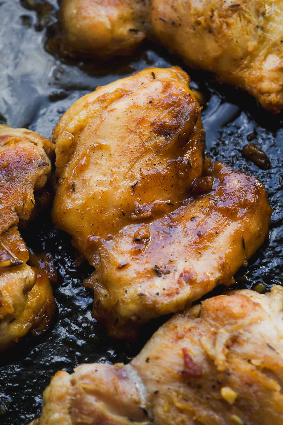 Close-up of golden-brown, seasoned chicken thighs cooking in a pan, with a glossy, slightly caramelized surface indicating they are being seared or roasted.