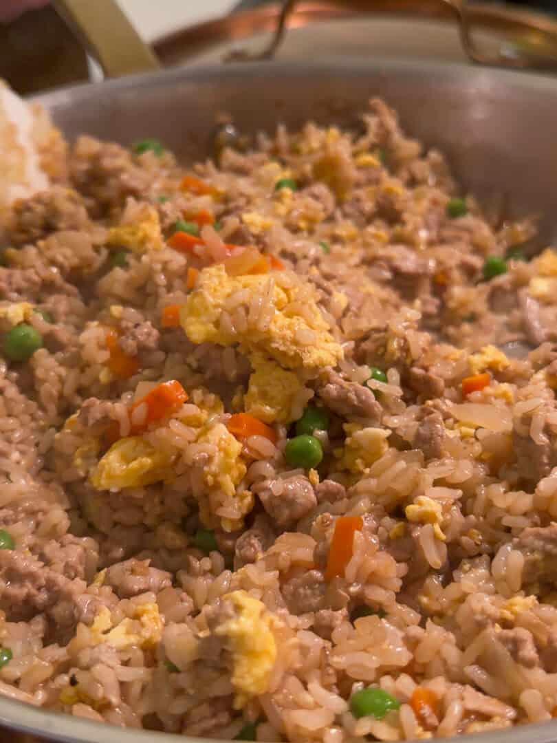 A close-up of fried rice with ground meat, scrambled eggs, peas, and diced carrots in a pan.