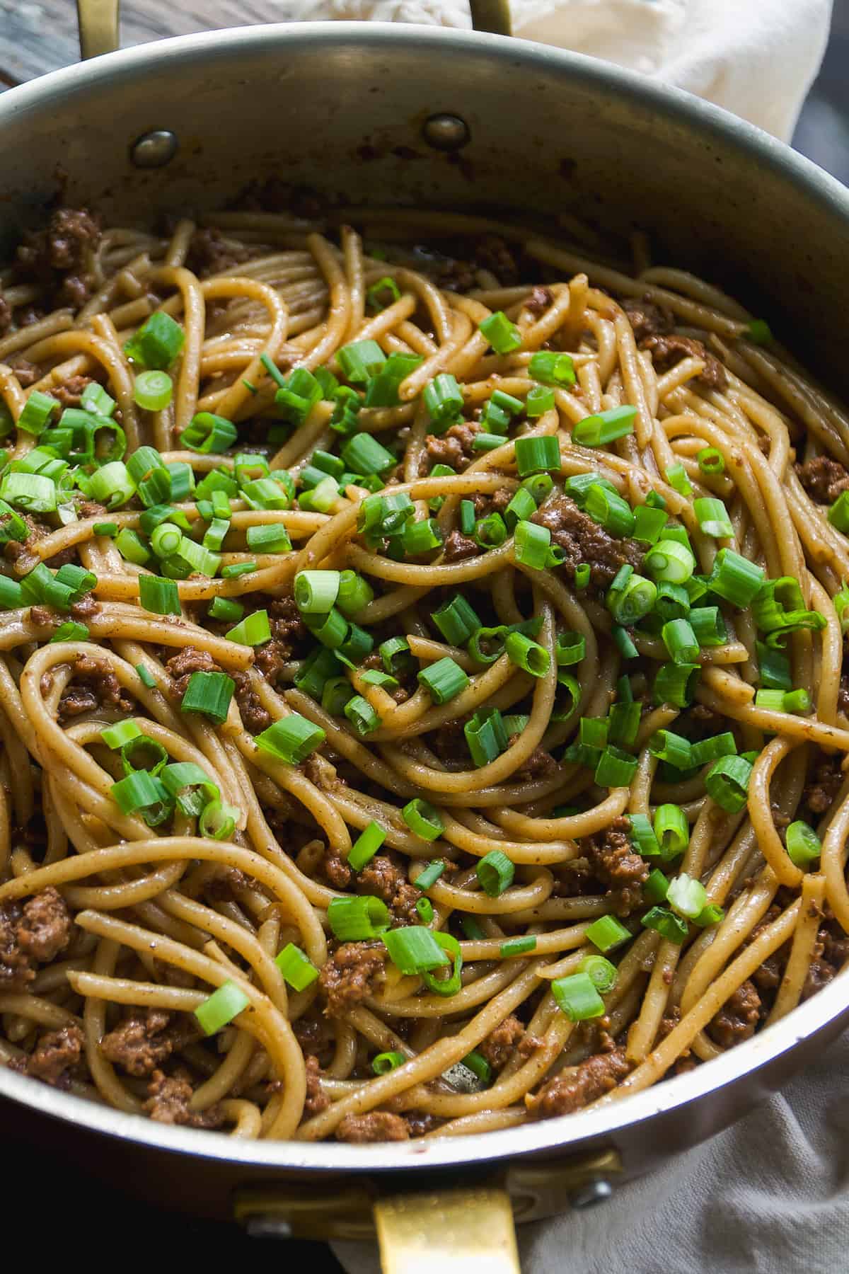 A large pan filled with cooked spaghetti mixed with ground beef and topped with chopped green onions. The dish appears savory and well-seasoned, with the pasta coated in a brown sauce.