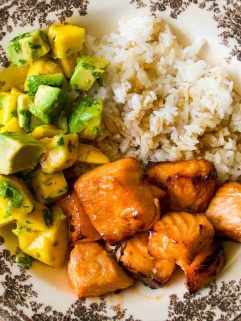 A decorative plate with grilled salmon chunks, white rice, and a salad of diced mango, avocado, and cilantro.