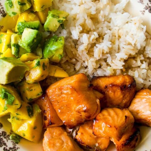 A decorative plate with grilled salmon chunks, white rice, and a salad of diced mango, avocado, and cilantro.