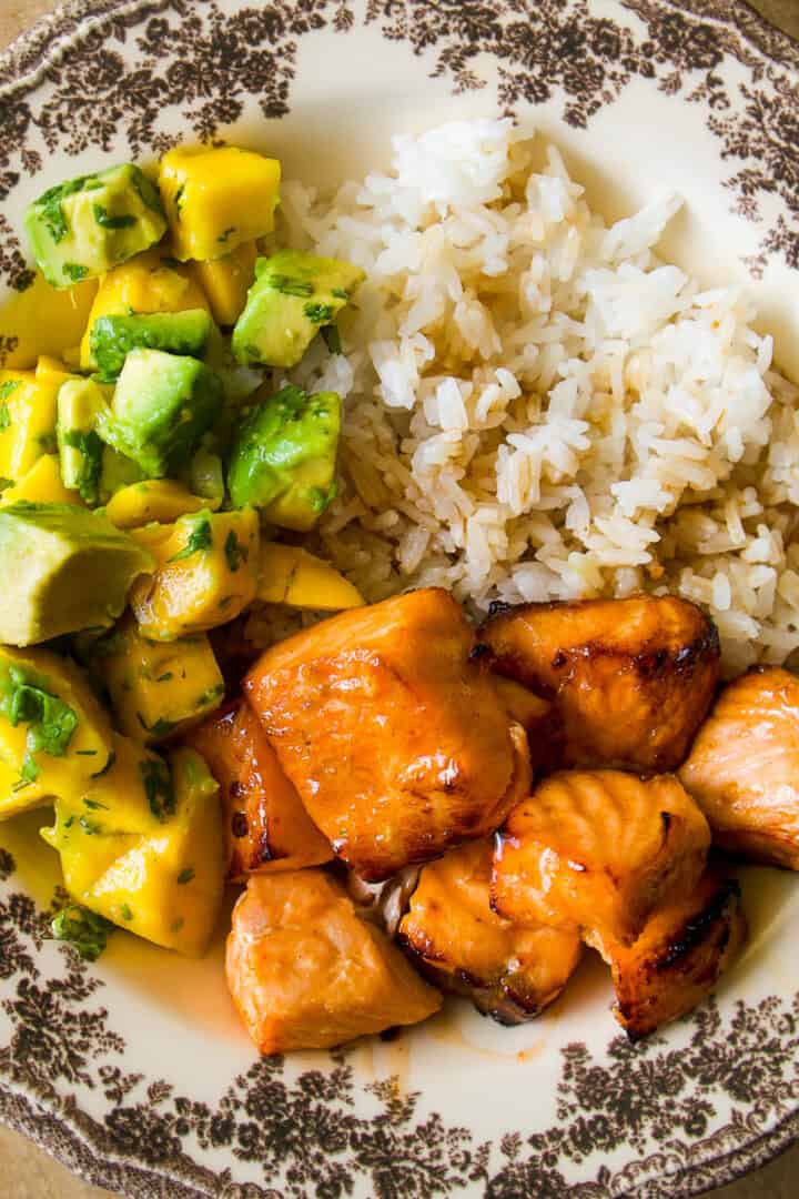 A decorative plate with grilled salmon chunks, white rice, and a salad of diced mango, avocado, and cilantro.