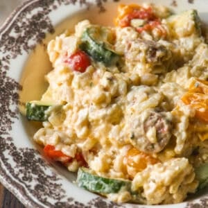A close-up of creamy rice mixed with sliced zucchini, cherry tomatoes, and mushrooms served on a decorative plate.