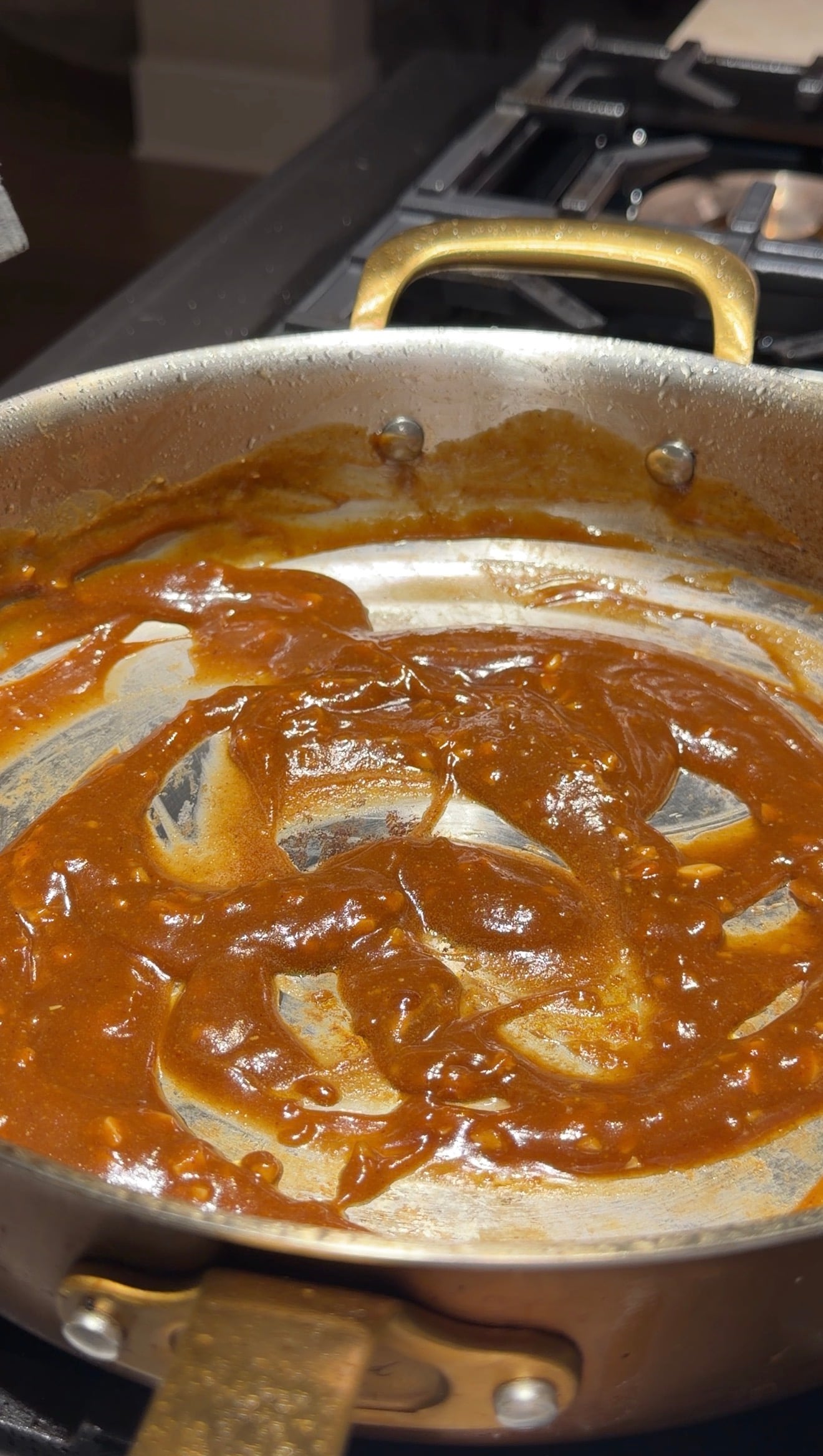 A pan with a thick, reddish-brown sauce, partially spread and scraped, showing streaks on the metal surface.