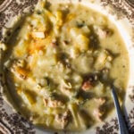 A bowl of creamy potato and sausage soup in a decorative patterned bowl with a metal spoon.