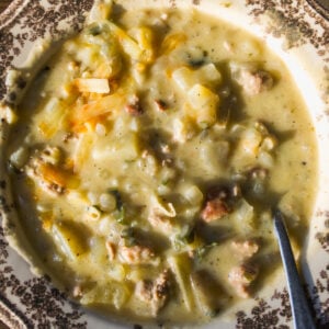 A bowl of creamy potato and sausage soup in a decorative patterned bowl with a metal spoon.
