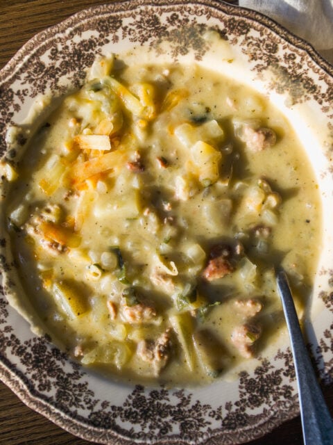 A bowl of creamy potato and sausage soup in a decorative patterned bowl with a metal spoon.