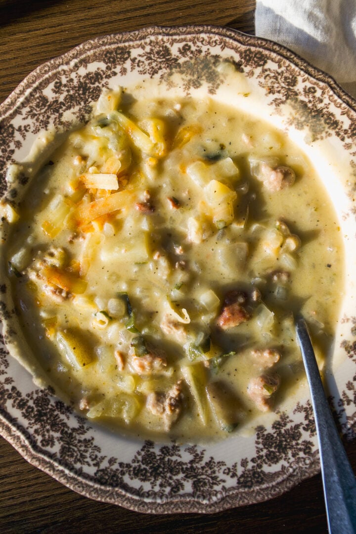 A bowl of creamy potato and sausage soup in a decorative patterned bowl with a metal spoon.