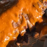 A rack of ribs coated in thick, orange barbecue sauce on a foil-lined tray.