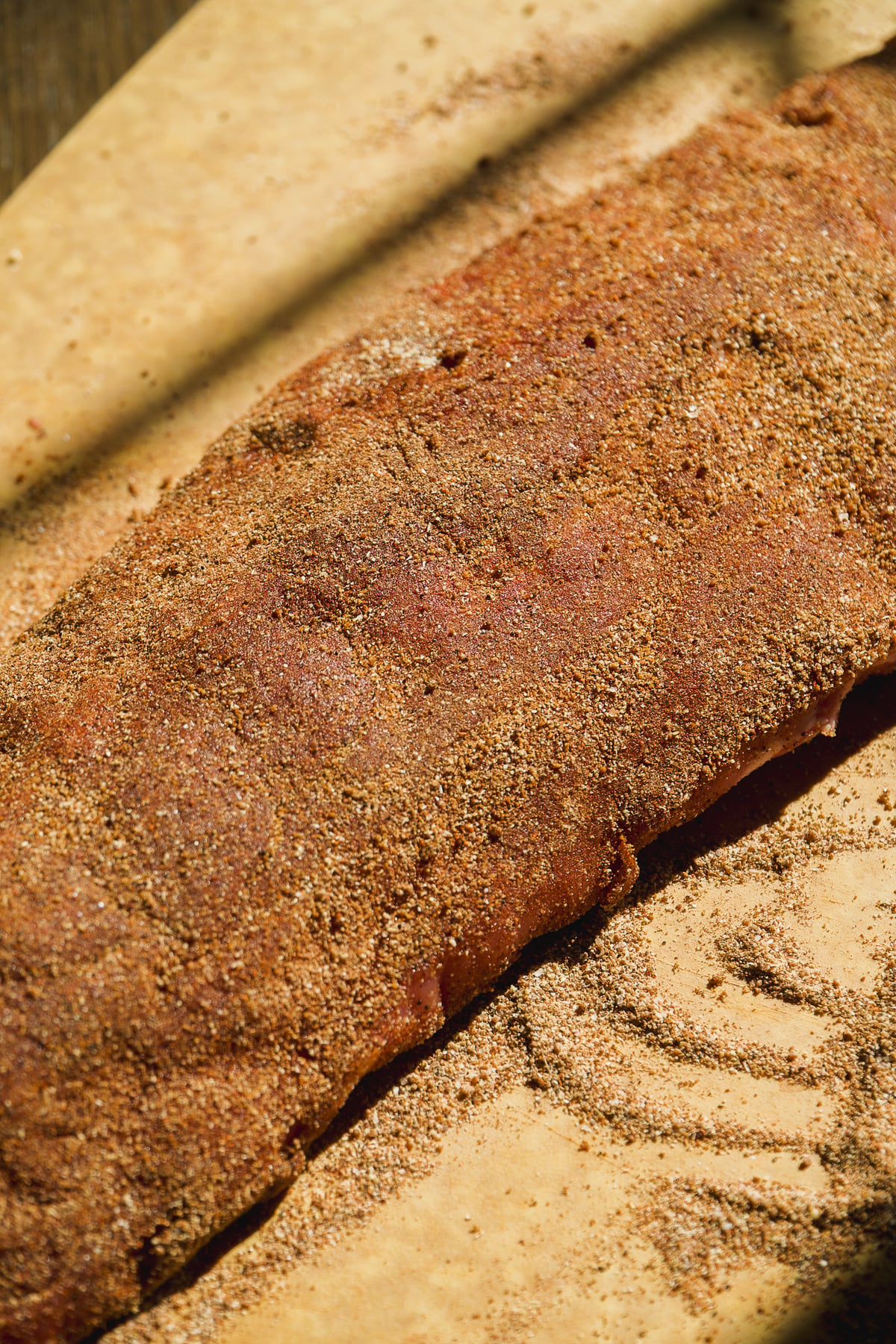 A rack of raw pork ribs coated in dry spice rub on parchment paper.