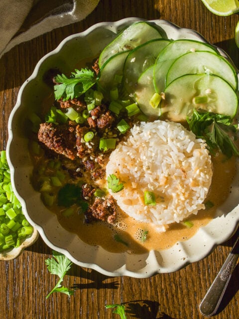 A bowl of ground meat and rice in a creamy sauce, topped with sliced cucumbers, green onions, and cilantro.