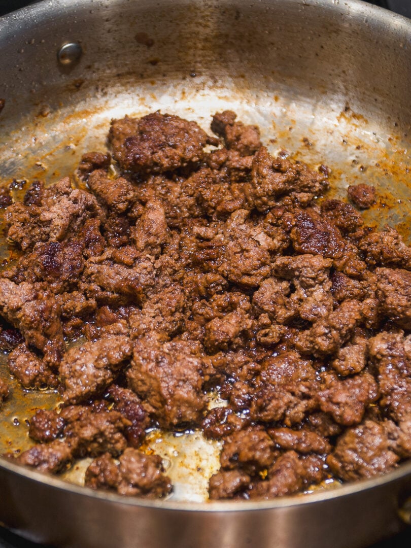 Ground meat browning in a stainless steel skillet.