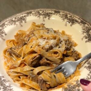 A fork twirls a portion of beef ragu tagliatelle topped with grated cheese in a decorative bowl.