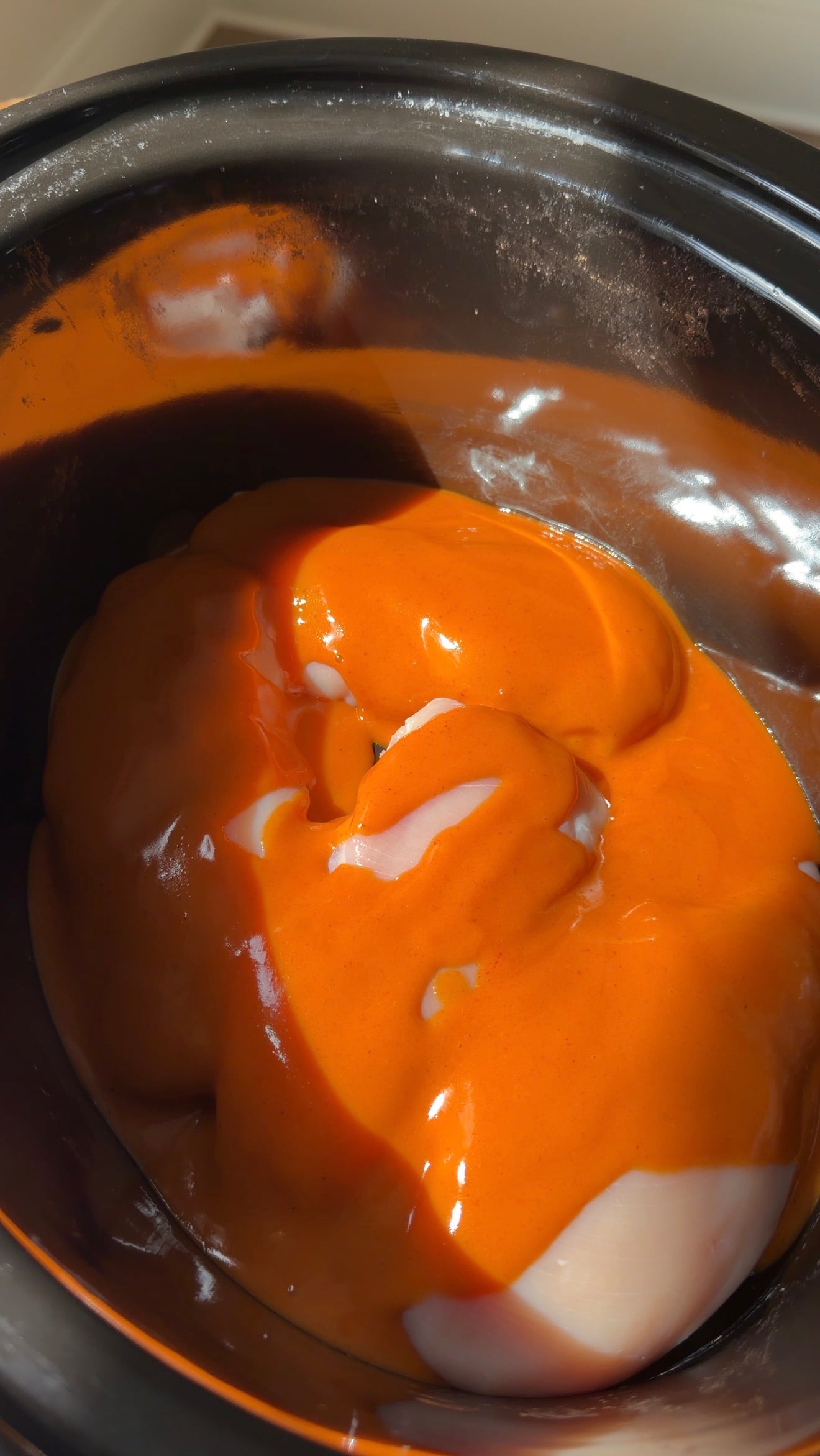 Raw chicken breasts coated in orange sauce inside a slow cooker.