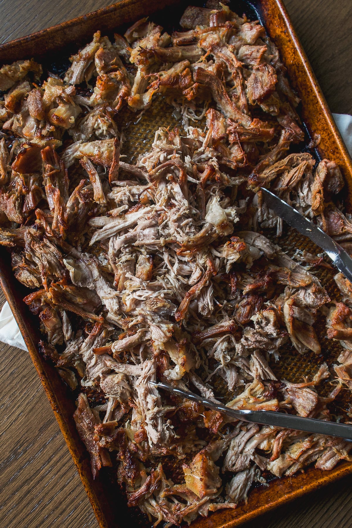 Pulled pork on a baking sheet with metal serving tongs.