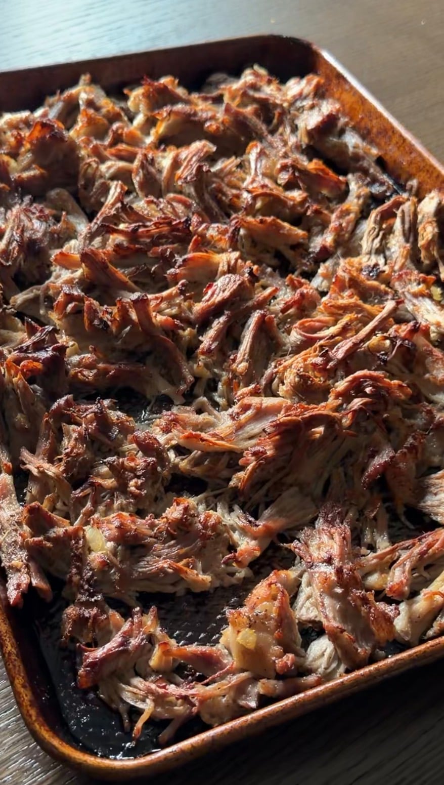 A baking sheet filled with shredded, browned pulled pork.