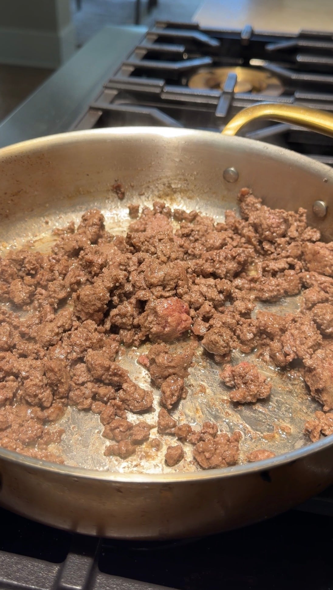 Ground meat browning in a stainless steel skillet on a stovetop.