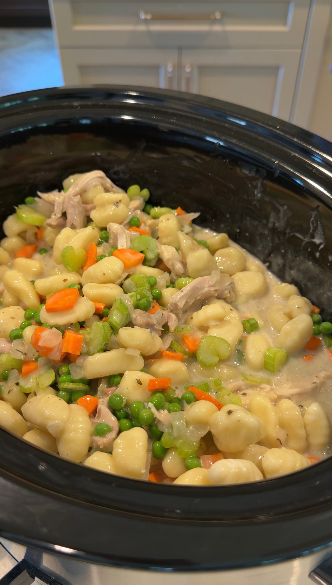 Chicken and gnocchi stew with peas, carrots, celery, and a creamy sauce in a black slow cooker, ready to serve.
