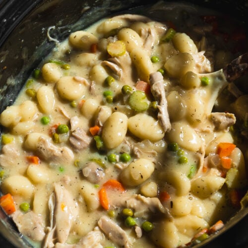 Creamy Crockpot Chicken Pot Pie Gnocchi stew with peas, carrots, and celery in a black slow cooker. This hearty dish is thick and full of tender vegetables and pillowy gnocchi.