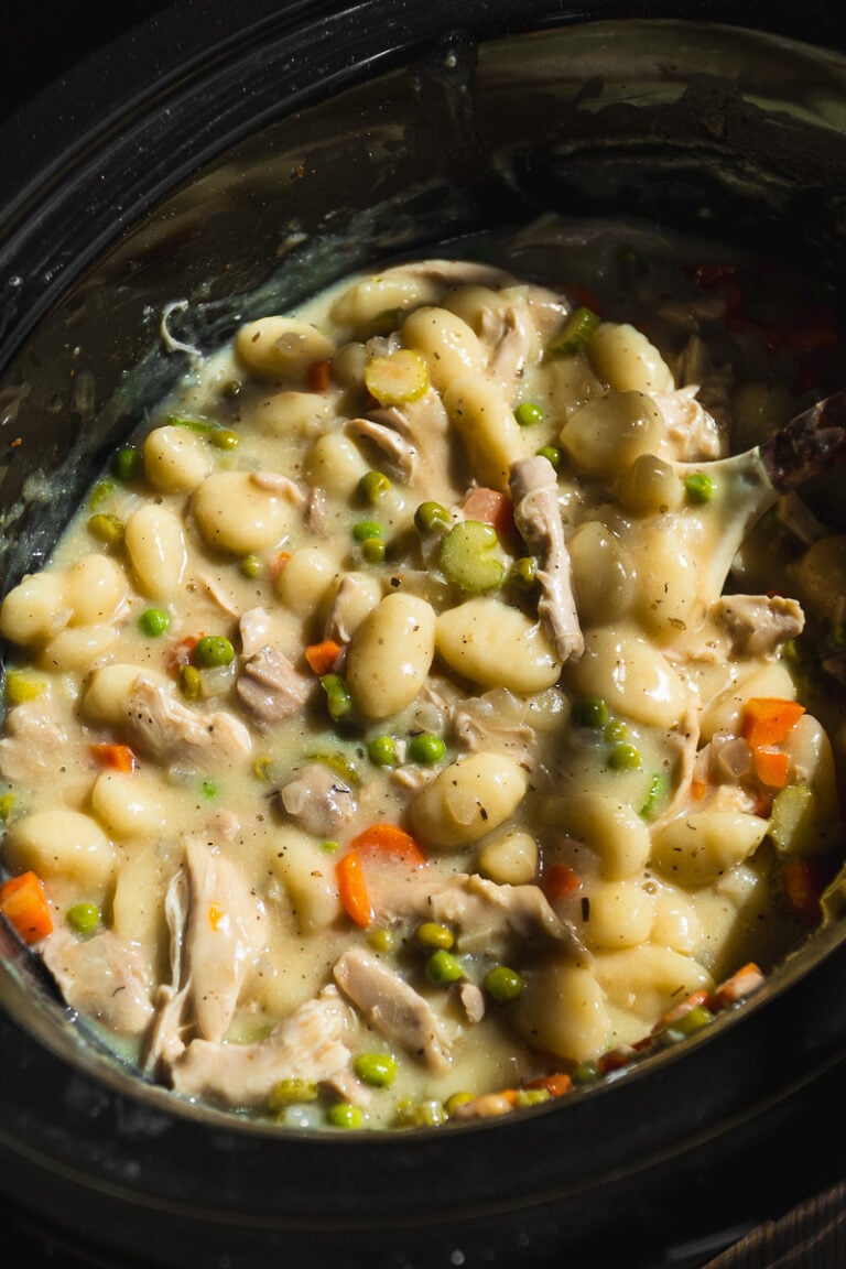 Creamy Crockpot Chicken Pot Pie Gnocchi stew with peas, carrots, and celery in a black slow cooker. This hearty dish is thick and full of tender vegetables and pillowy gnocchi.