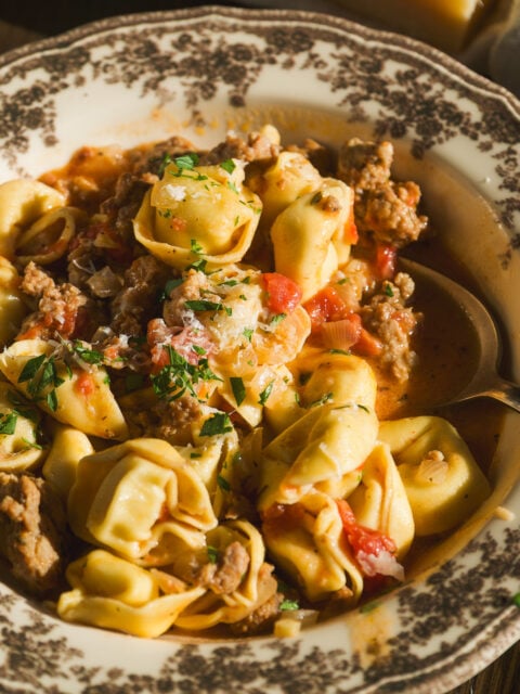 A bowl of tortellini with meat sauce, garnished with herbs and grated cheese.