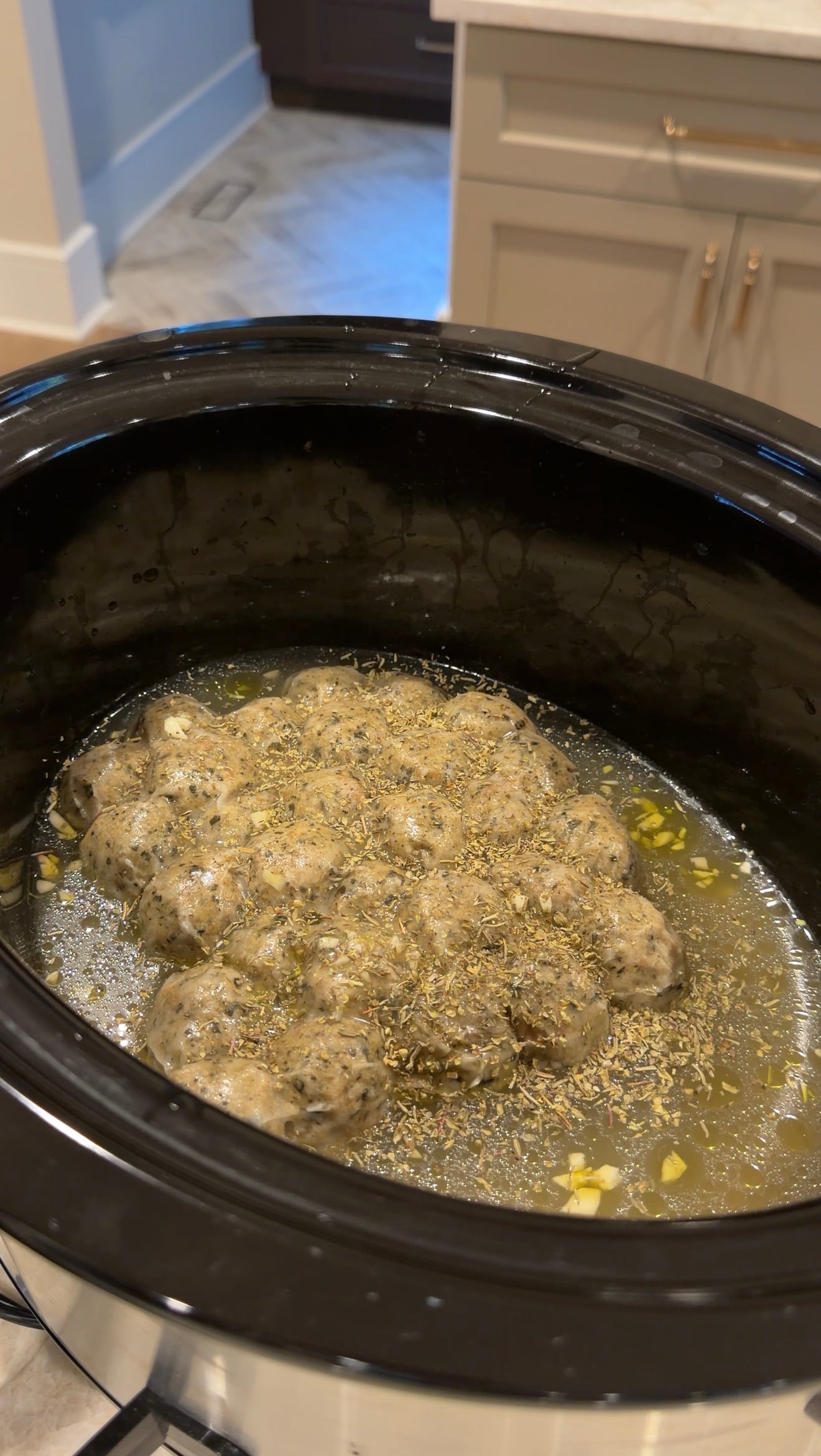 Meatballs cooking in a slow cooker with broth and dried herbs.