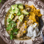 A bowl of chicken and rice soup topped with diced avocado, crushed tortilla chips, cilantro, and a dollop of sour cream.
